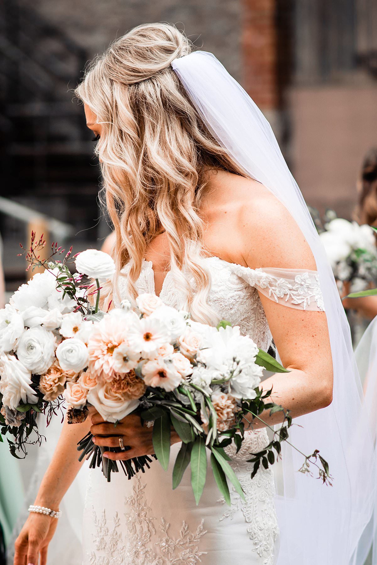Bride holding her neutral colored bouquet and looking away from camera over her shoulder towards her bridesmaids