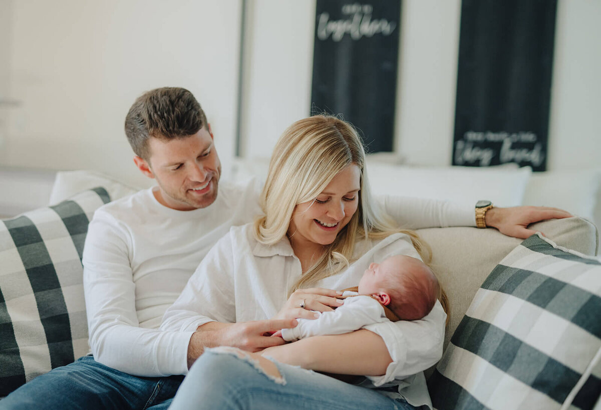 Couple sitting on sofa looking at newborn  baby at newborn photoshoot at Finger Lakes, NY
