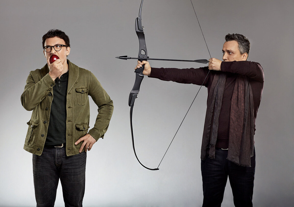 Playful portrait of Anthony and Joe Russo, with Joe aiming a bow and Anthony posing thoughtfully, captured in a Marvel-themed shoot by Ylva Erevall.