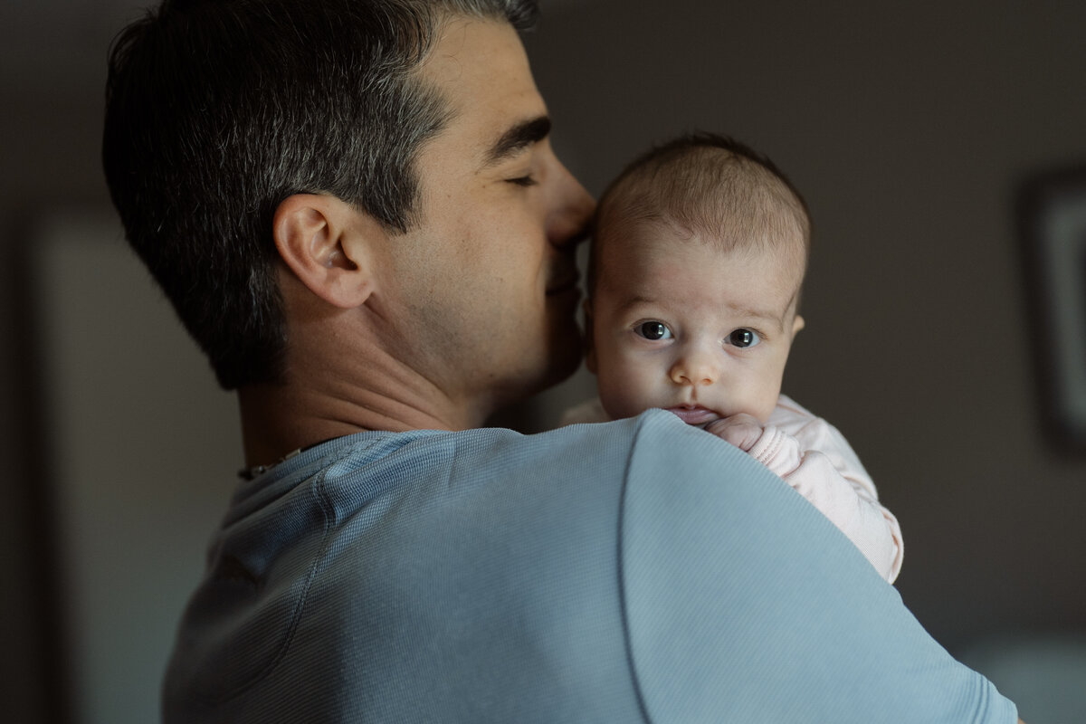 A sweet portrait of a father cradling his baby, symbolizing love and security during a lifestyle family session at their home in Fort Worth, Texas.