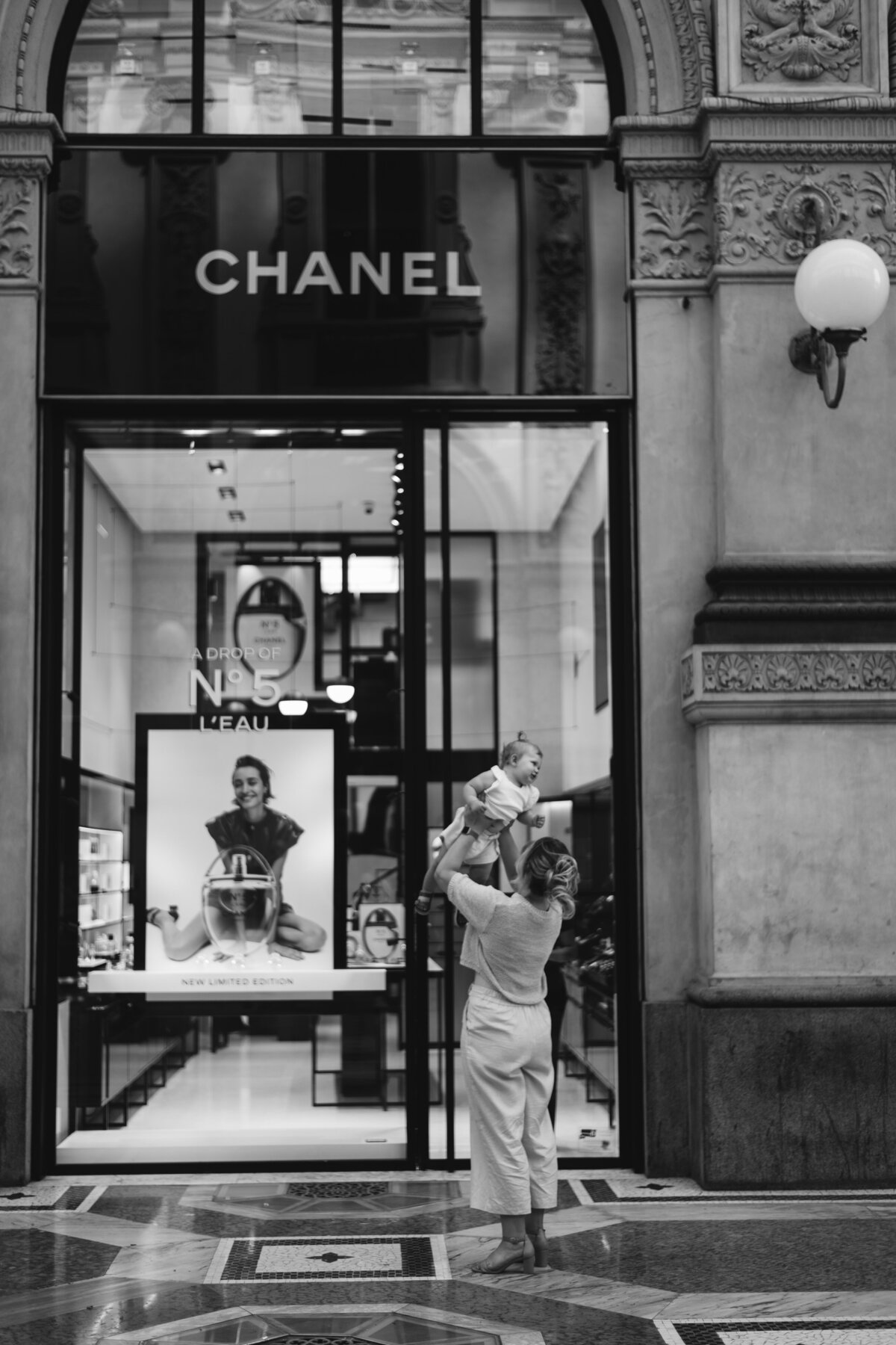 Mother gently holding child on steps of a Milanese storefront, embodying serene family connection
