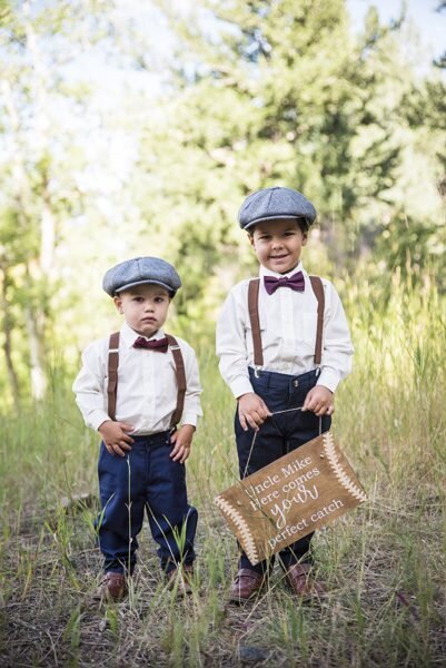 Two little boys act as ring bearers, wearing bow ties, suspenders and hats. One carries a clever sign.