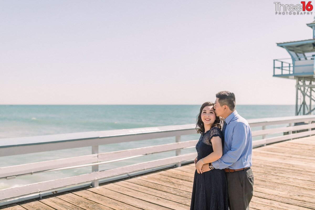 Groom to be whispers into his fiance's ear while standing on the San Clemente Pier