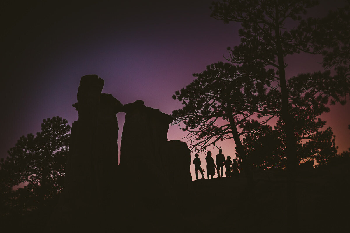 silhouette of colorado trees and mountains with a family standing in the middle during sunset