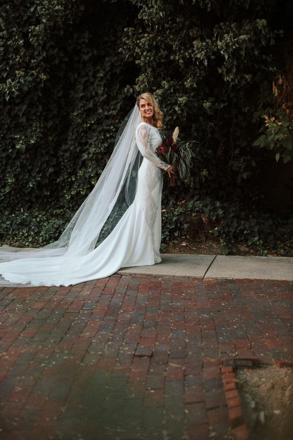 Bride on her wedding dress with a long veil and a burgundy and greenery bouquet.