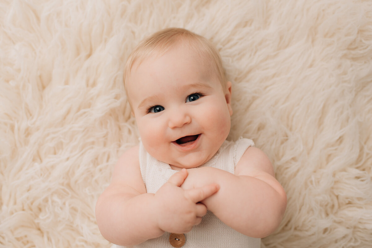 Baby boy smiling up at the camera, wearing white outfit on white backdrop