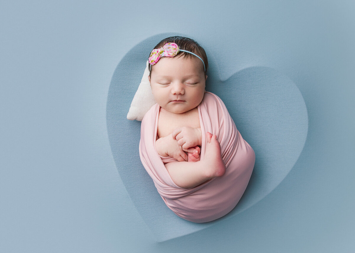 Newborn baby wrapped in pink wrap laying in heart shaped bowl during newborn photoshoot in Franklin Tennessee photography studio