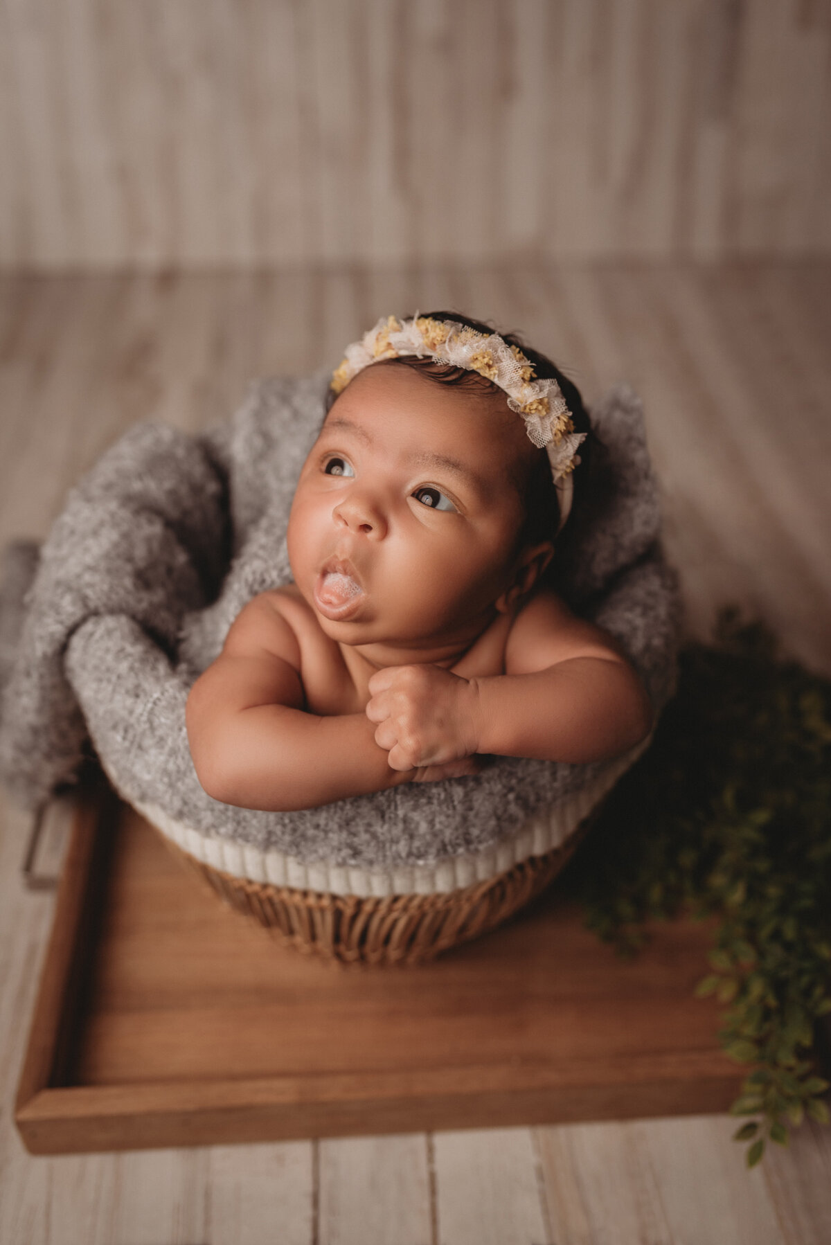 one month old baby girl posed for newborn portrait session at Atlanta, GA newborn photography studio sitting in basket with chin on hands wearing a flower headband