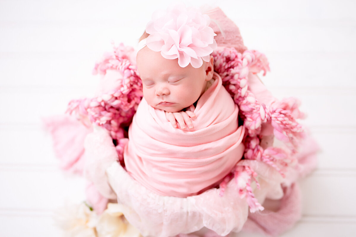 Newborn wrapped in pink blankets and nestled in a floral basket, captured in Overland Park, Kansas. A whimsical and charming setup for families looking for soft and feminine newborn photography themes.