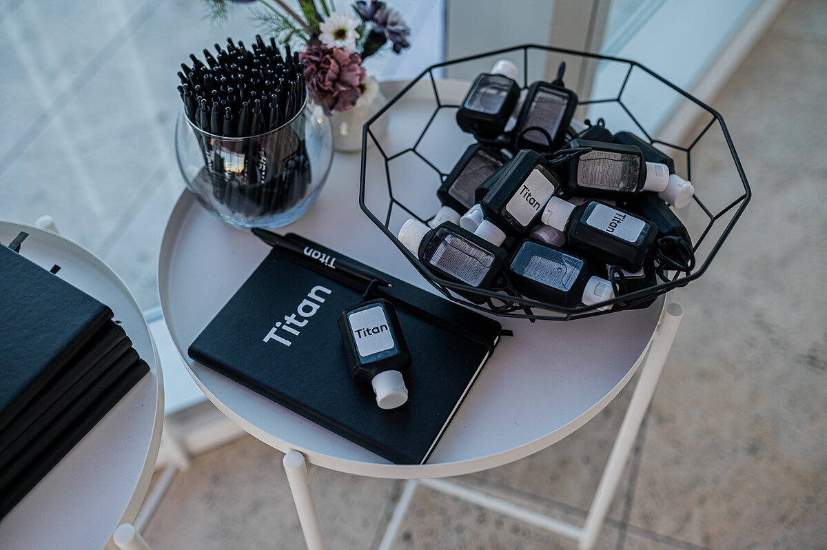 Titan-branded notebooks, pens, and hand sanitizers displayed as guest amenities at Titan Day in New York, produced as part of the high-end corporate event experience.