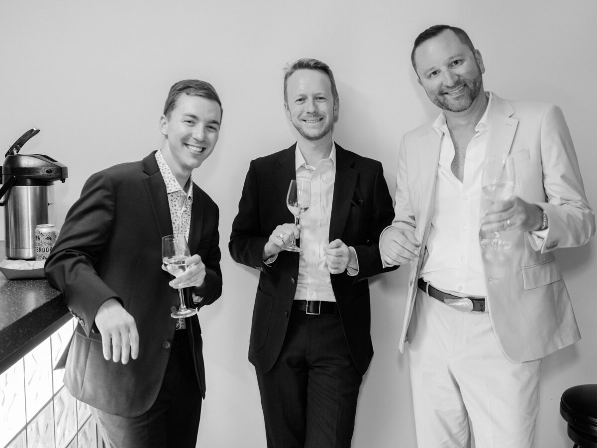 Three well-dressed men are enjoying a moment together while holding glasses, radiating celebration and camaraderie in a chic atmosphere filled with elegance.