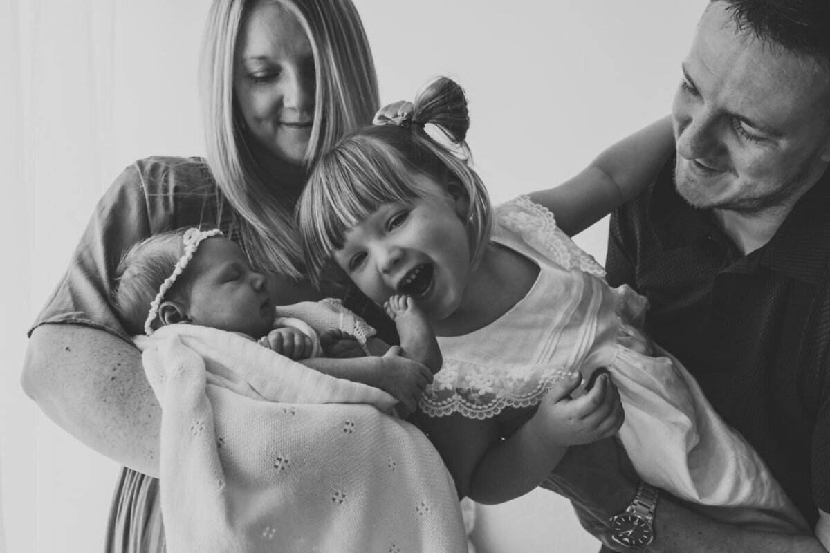 Parents adoringly hold their newborn baby and laughing older daughter. Lifestyle family photography