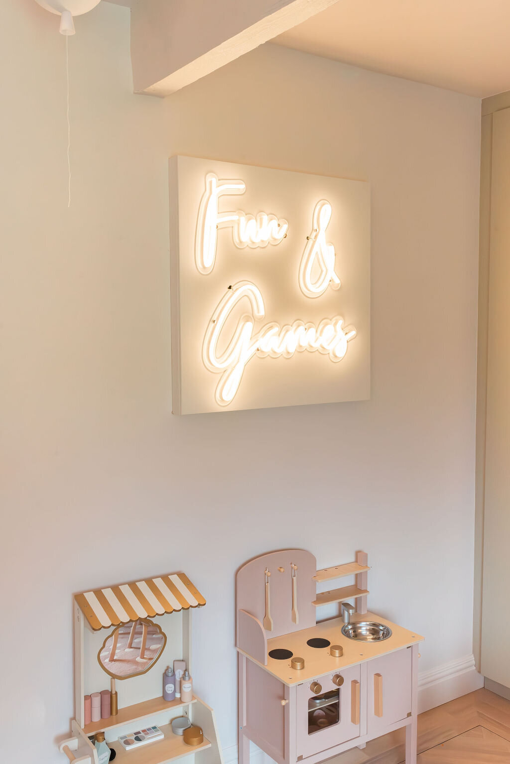 A soft neon sign in a children's playroom, above toys, reading 'Fun & Games'.