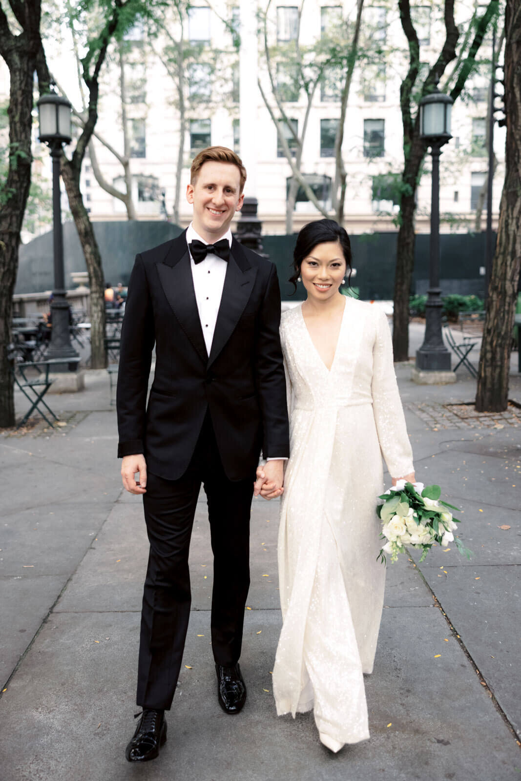The bride and the groom are smiling at the camera at the New York Public Library Park. Image by Jenny Fu Studio