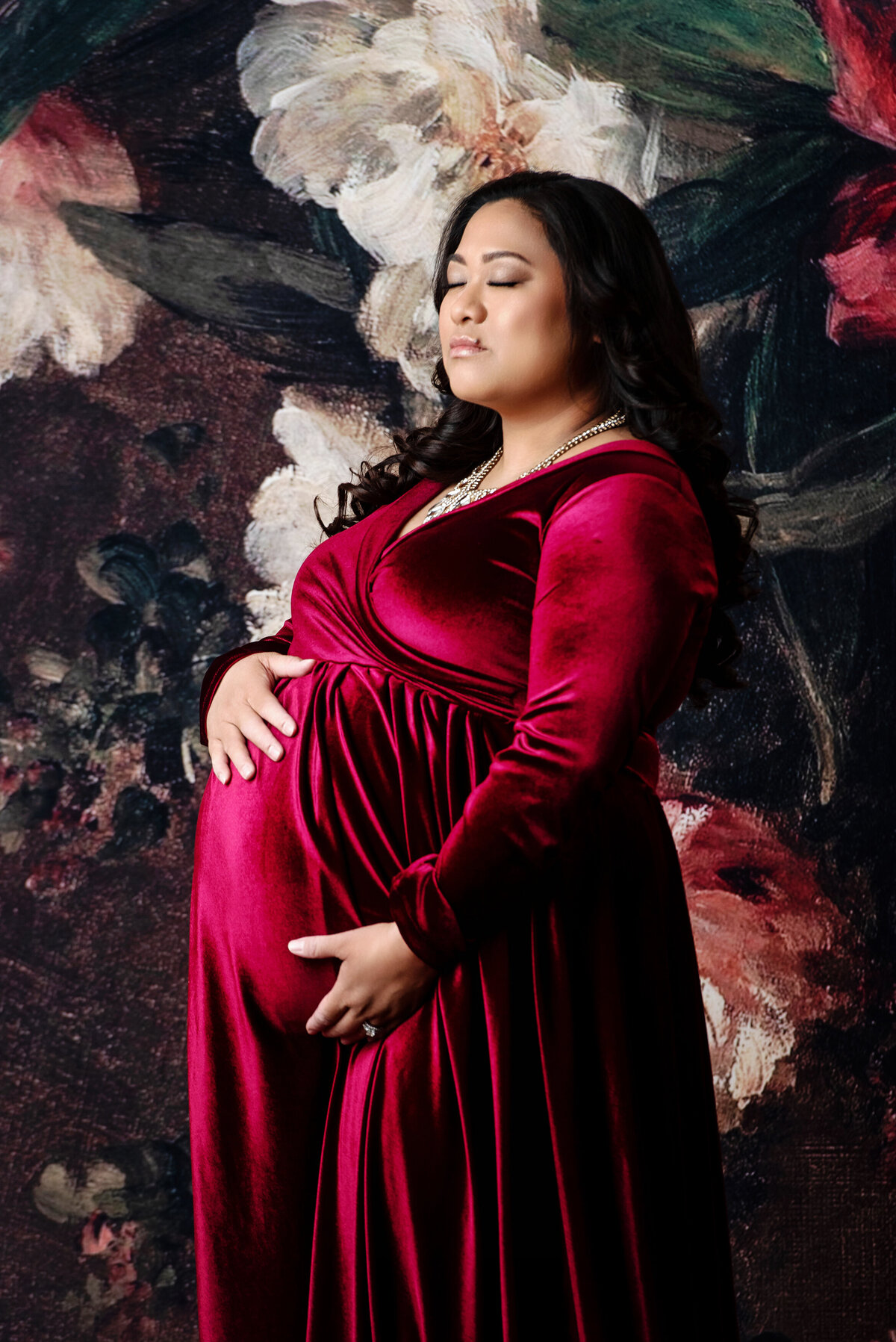 st-louis-maternity-photographer-mom-in-red-velvet-dress-on-red-and-cream-floral-backdrop