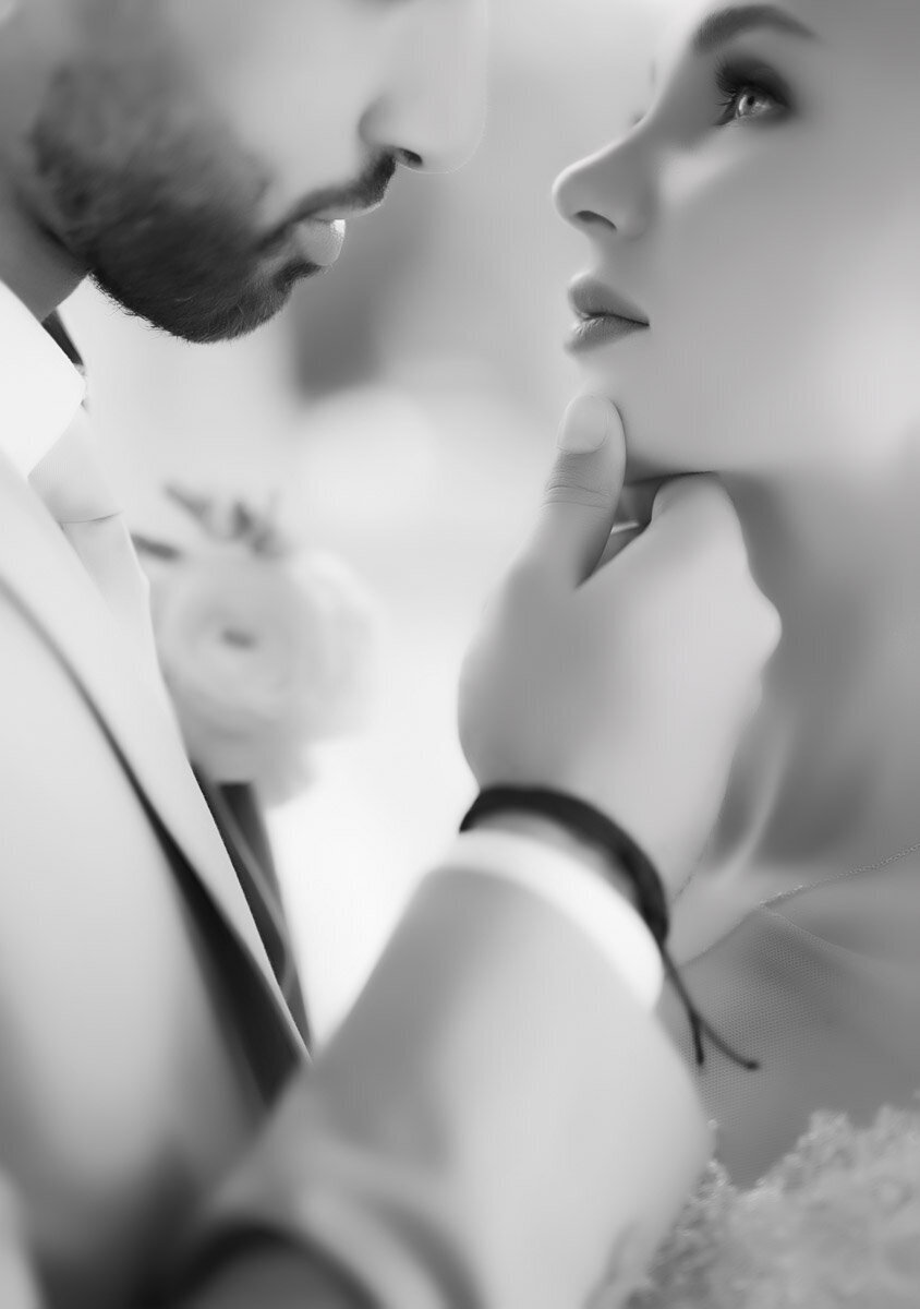 black and white wedding photo of groom holding brides chin, looking into each others eyes