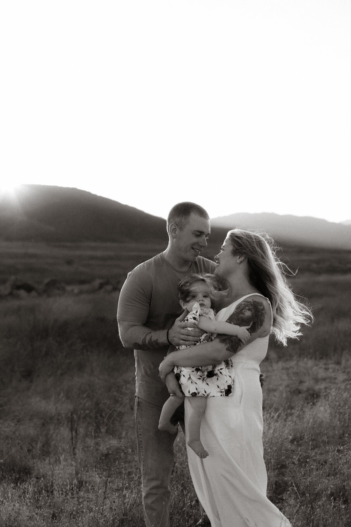 Family of three sharing a quiet moment in a sunlit field, with golden light illuminating their smiles.