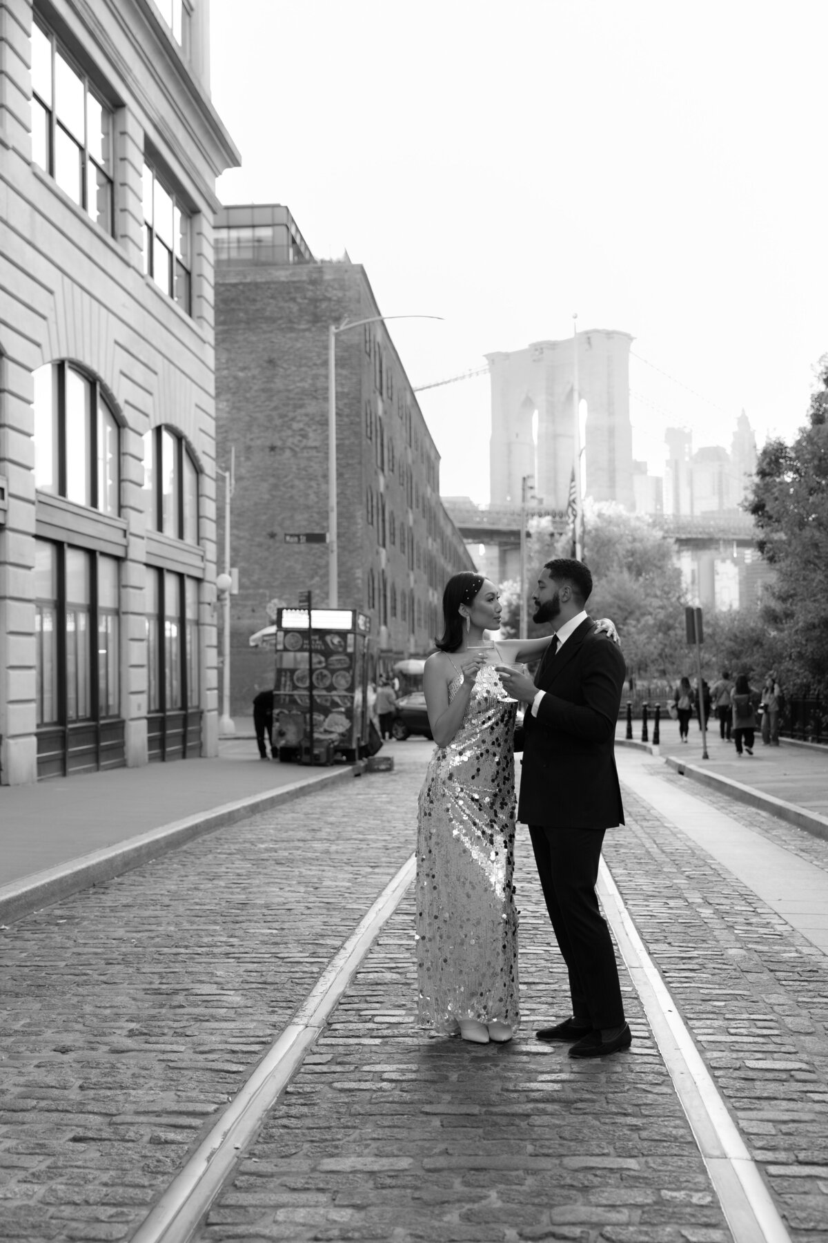 The couple embraces near the base of the Brooklyn Bridge, surrounded by the DUMBO neighborhood's textures.