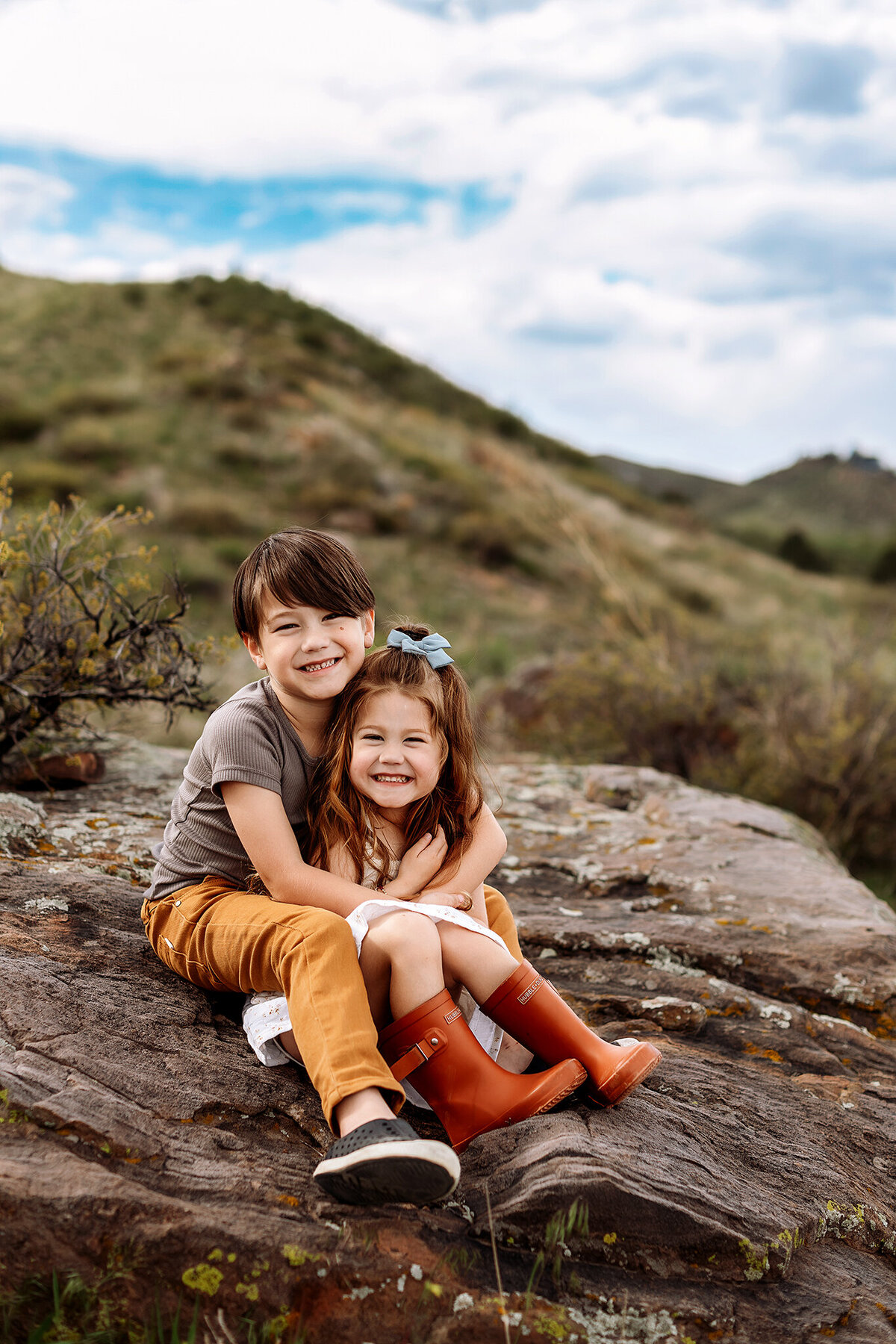 siblings hugging on a rock in the mountains during their family photos in denver