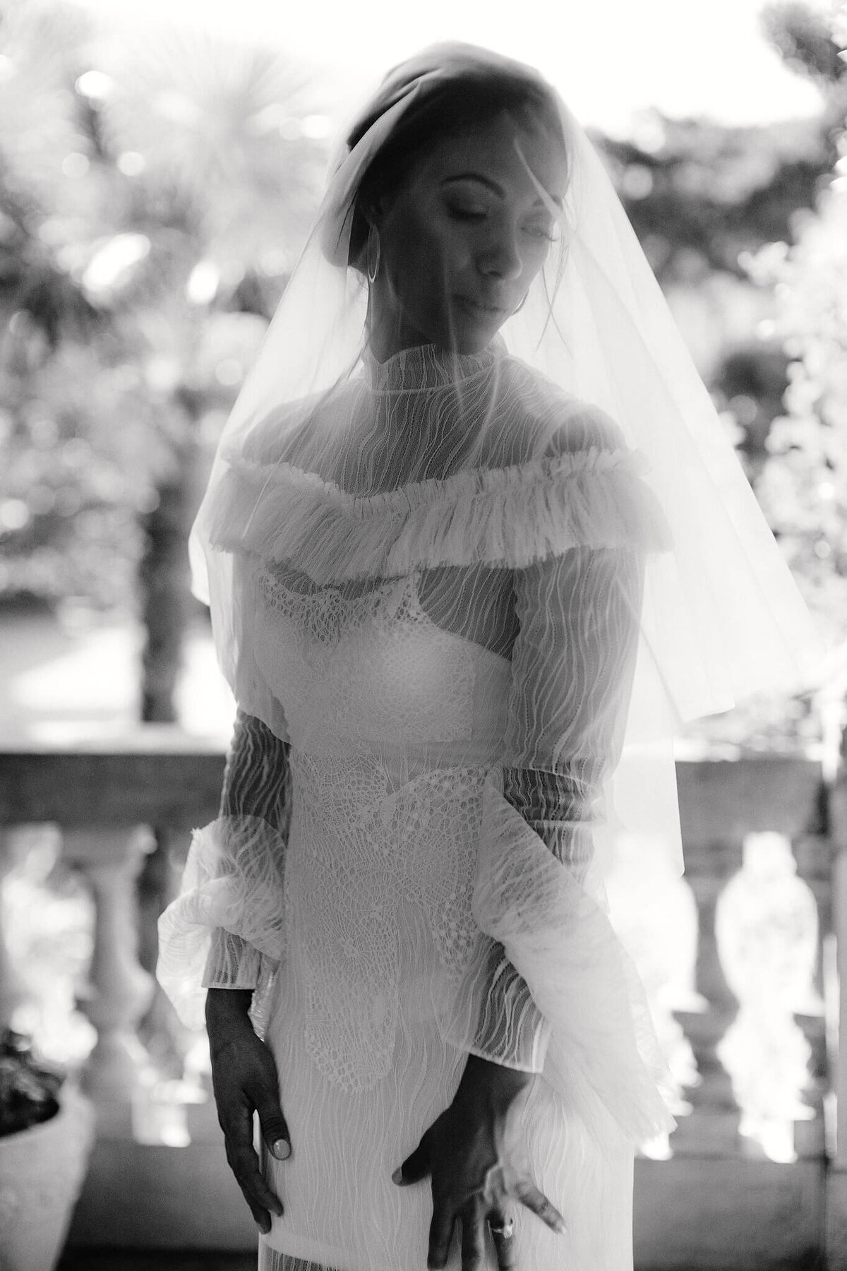 Close-up, half-body shot of a bride while standing, with both hands in front of her legs as she looks down to her left side