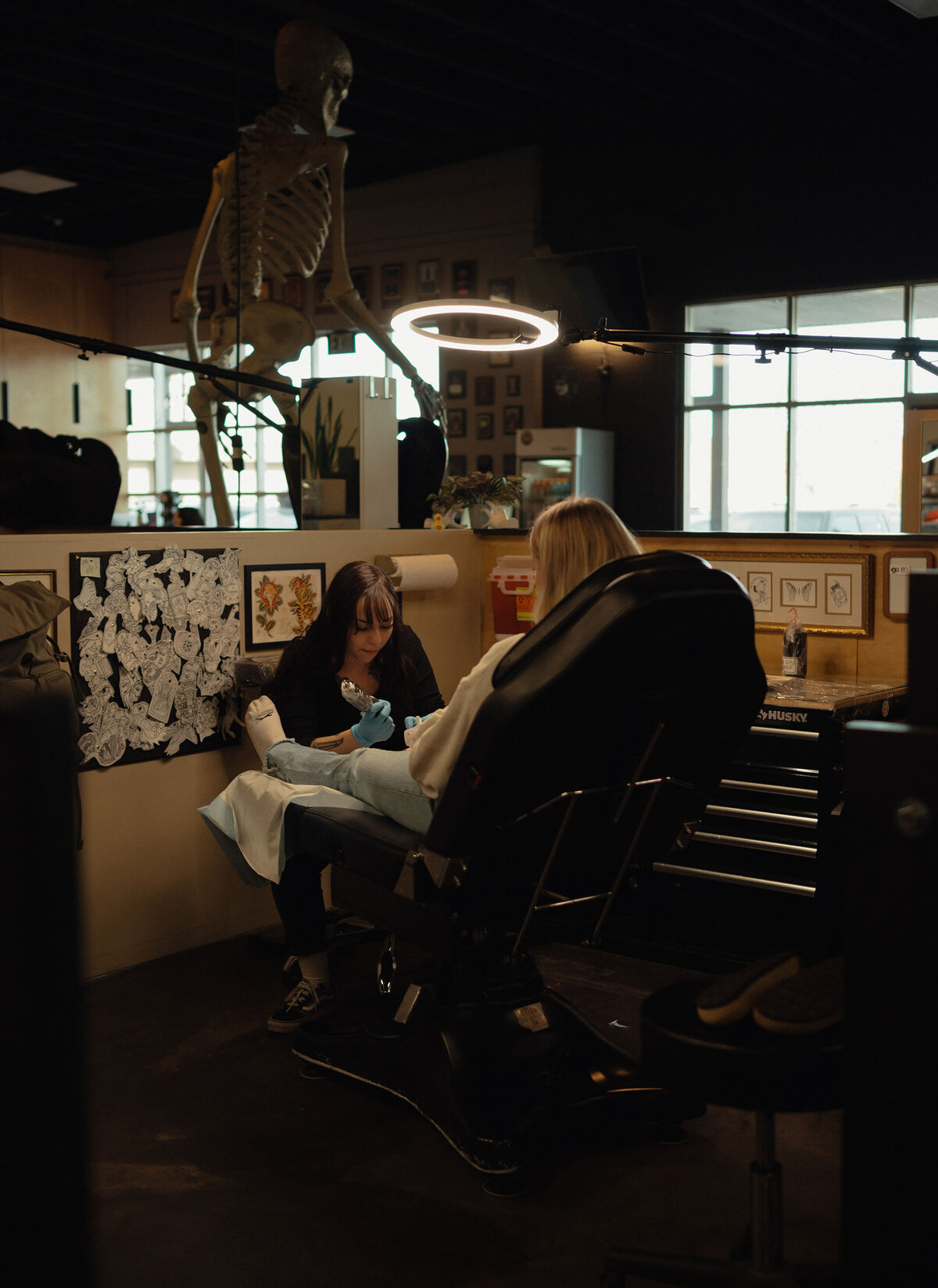 female tattoo artist is giving a tattoo to a client in a moody and dim lit studio during a personal branding photoshoot in Oregon