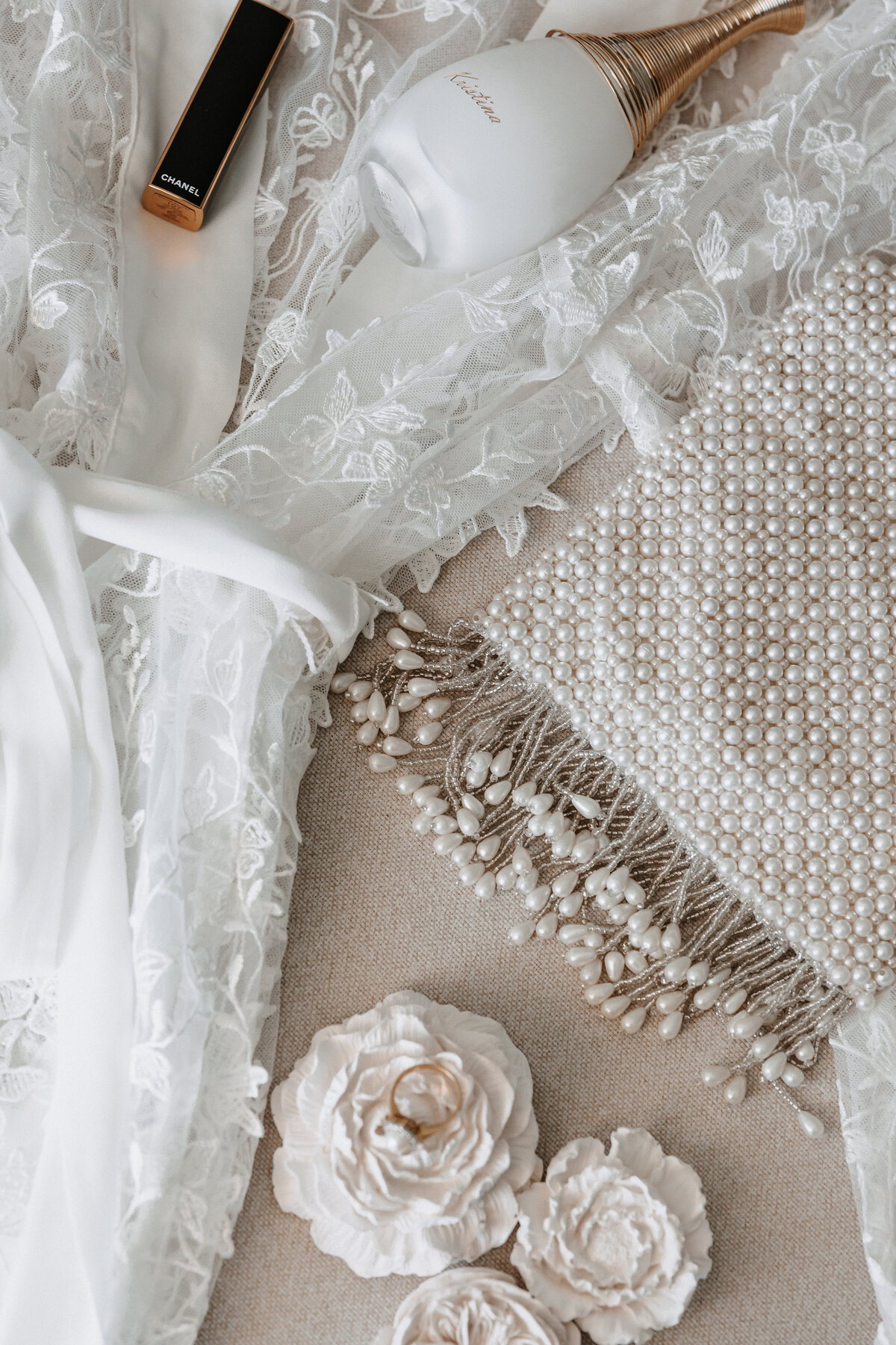 flat lay detail photo of wedding ring, lipstick, perfume, purse and robe