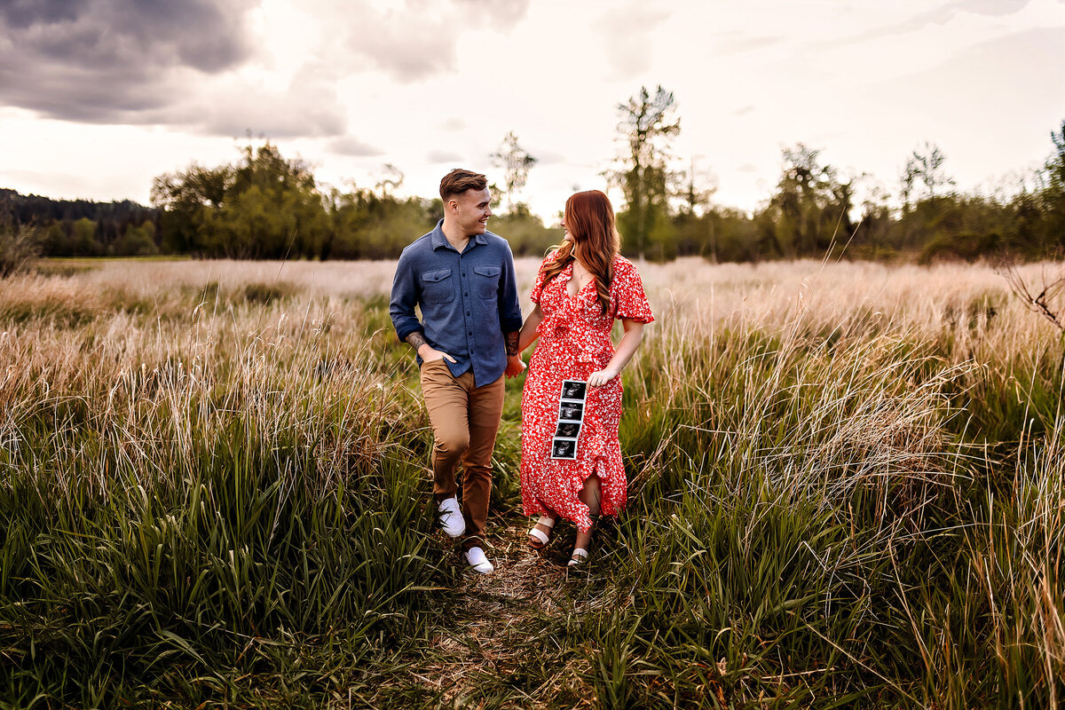 Soon to be mom and dad walk through grassy fields to announce their pregnancy journey