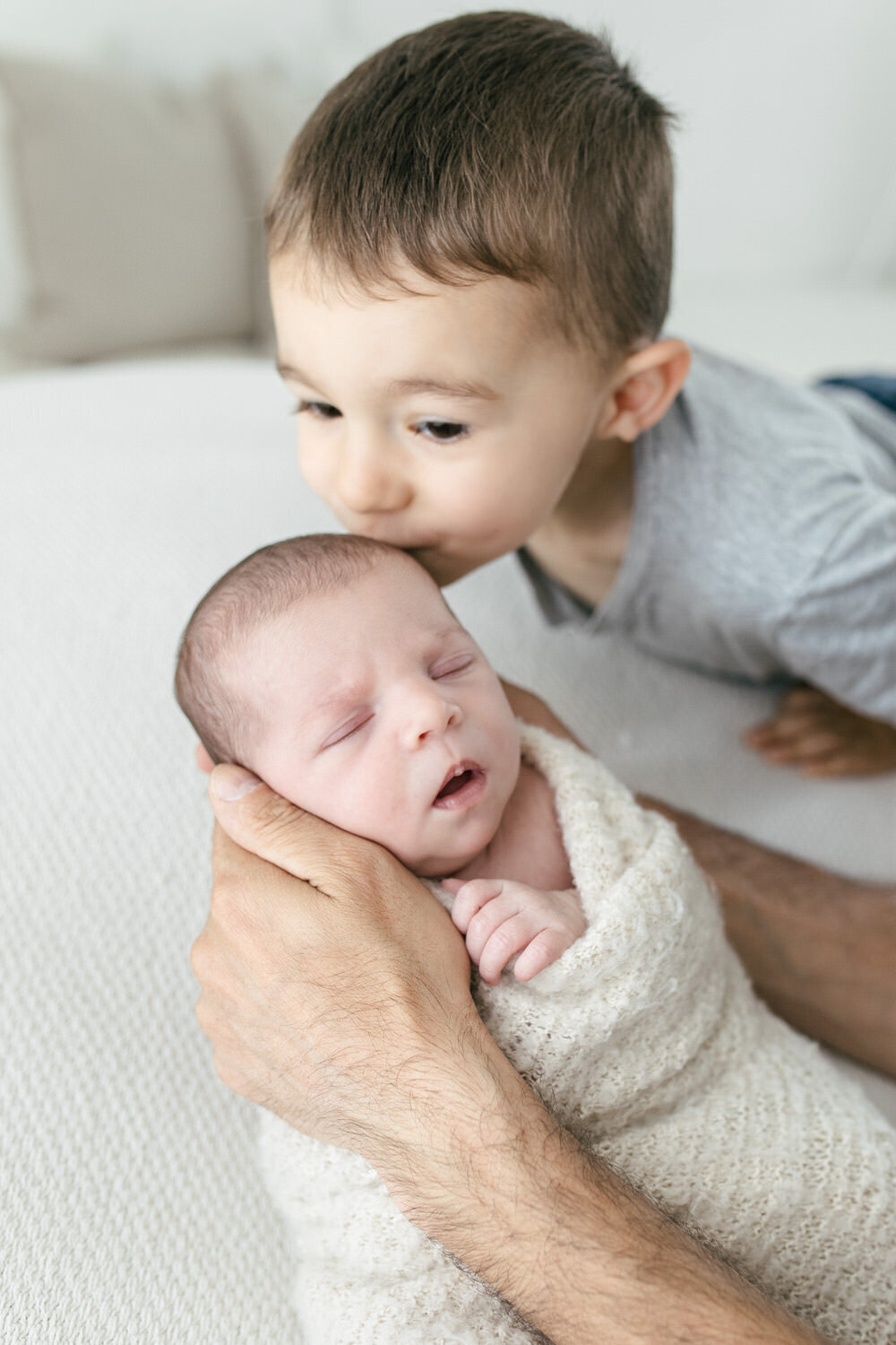 Big brother kisses newborn sibling on the side of the head