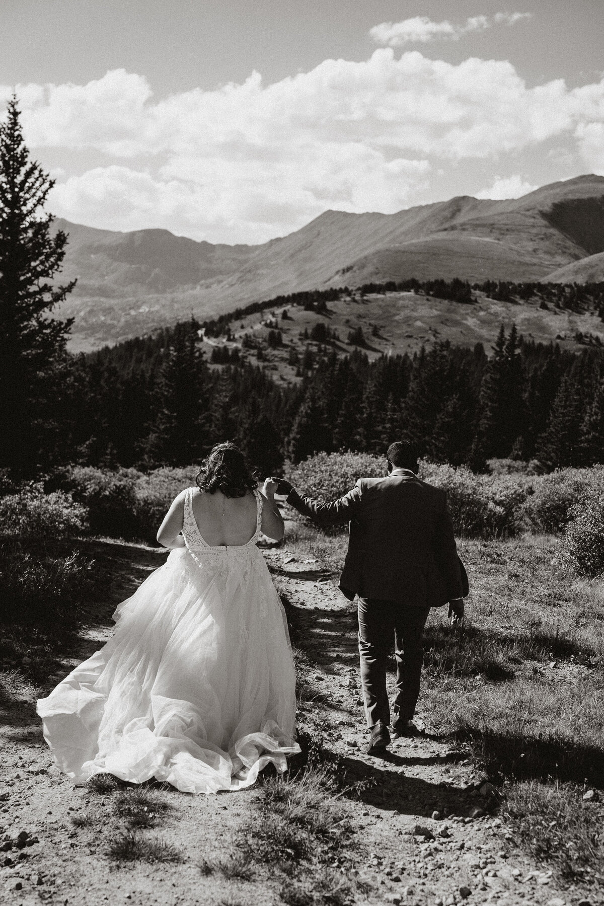 Bride and groom walk hand in hand on rugged trail after mountain elopement near in Hoosier Pass.