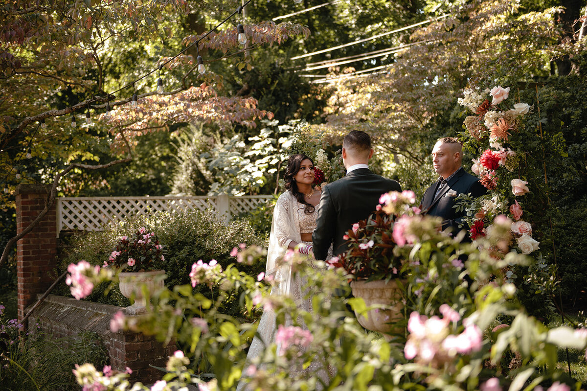 The couple standing before a floral arch, framed by a charming backyard garden and soft natural light.