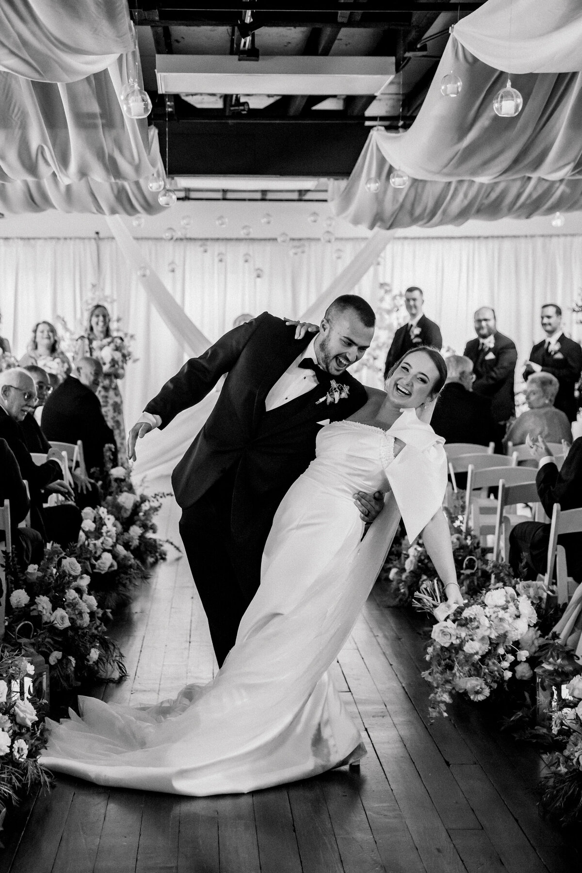 Bristol Train Station Wedding in Bristol, VA | Film Wedding Photographer - Caitlin Wilcox | black and white image of bride being dipped by groom in the middle of their aisle as they recess after their ceremony - links to feature gallery page for a summer wedding at the Bristol Train Station
