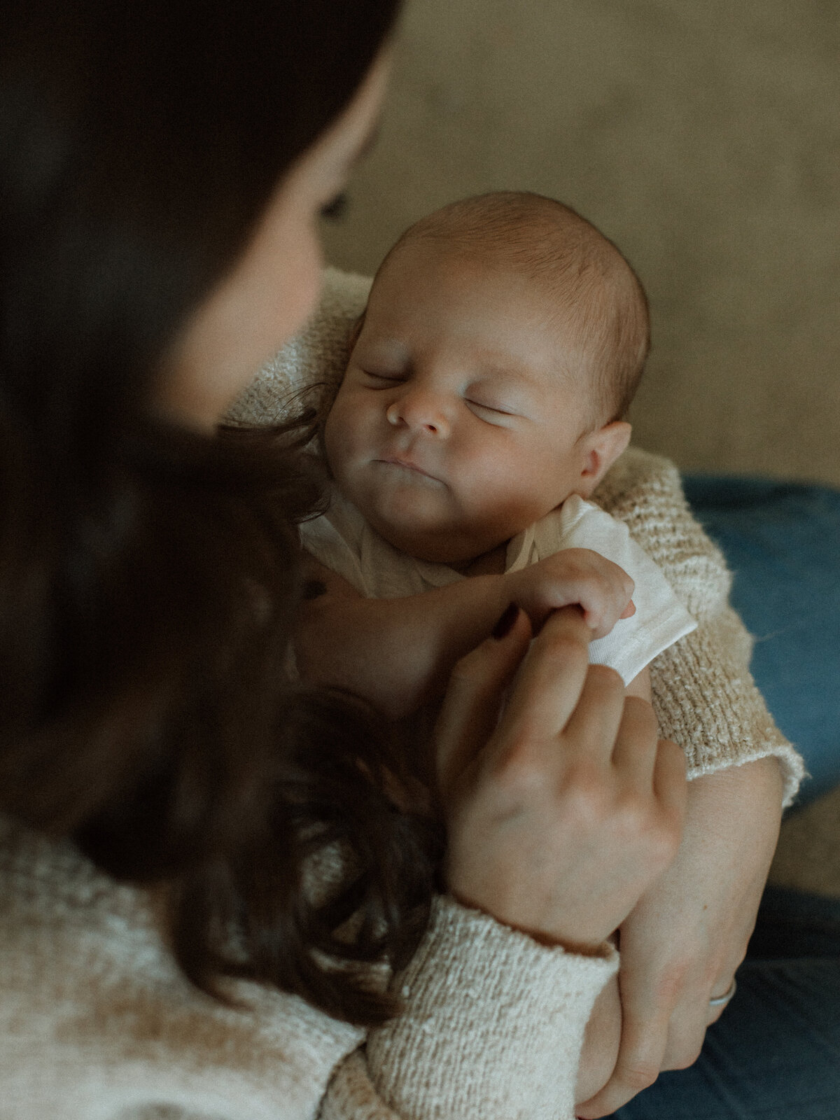 Newborn cradled in mom's arms while gently grabbing mom's index finger while sitting on the floor.