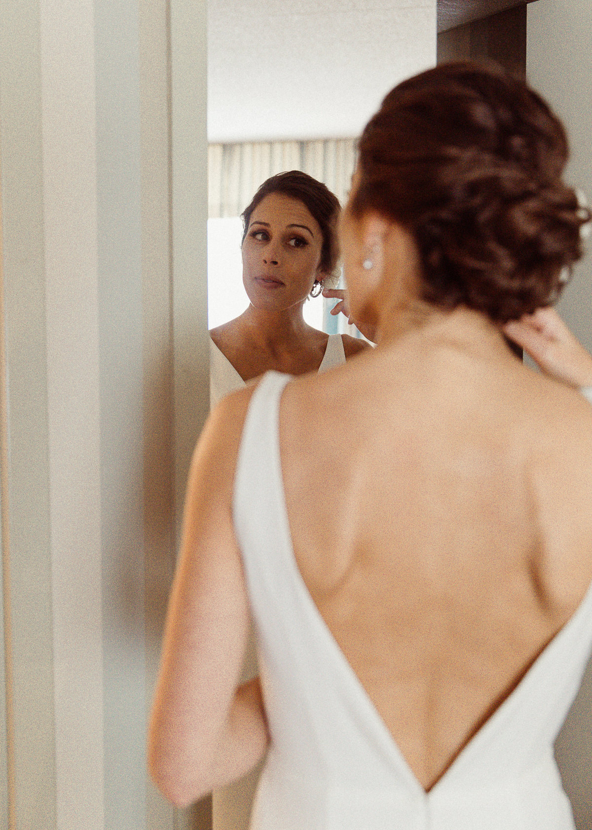 bride putting in earring with a view of her backless wedding dress