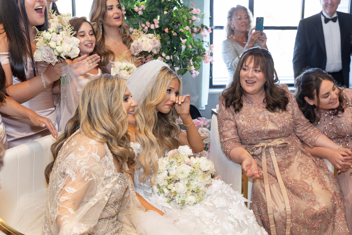 A bride wiping tears as she sits with wedding guests