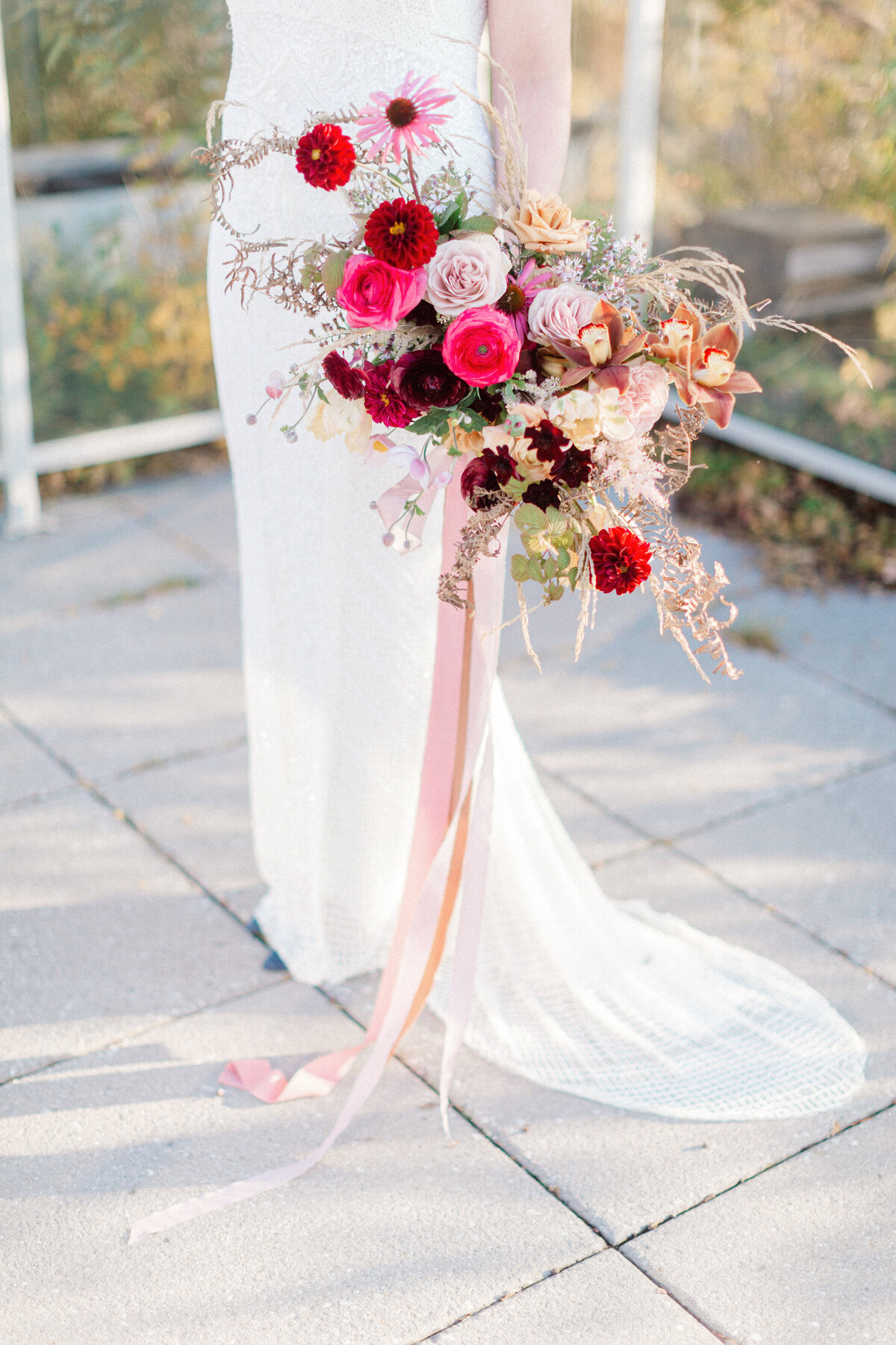A bride holds a lush bouquet of red flowers tied with a long pink ribbon at Stonehaven Manor.