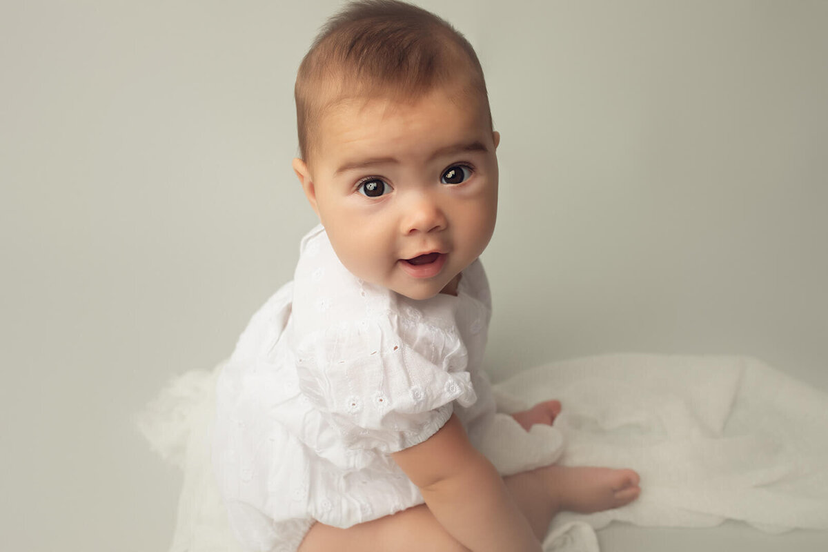 a close up shot of a six month old girl wearing a white romper