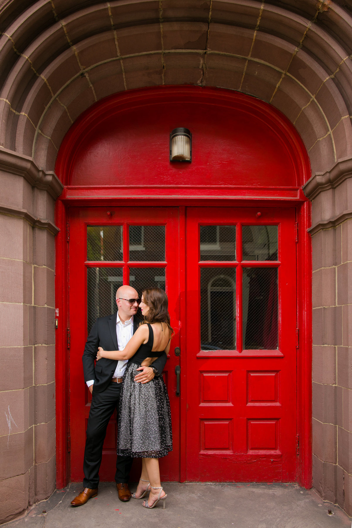 An engaged couple posing in front of a bold, graphic red door in Philadelphia during their engagement session, creating a vibrant and modern backdrop that highlights their unique love story.