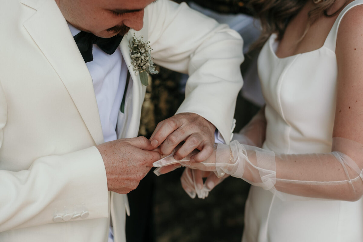 Der Bräutigam steckt der Braut ihren Ehering an die behandschuhte Hand.