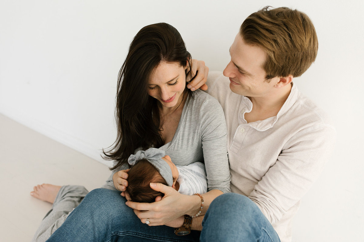 Neutral newborn session, father looking at his wife holding their new baby