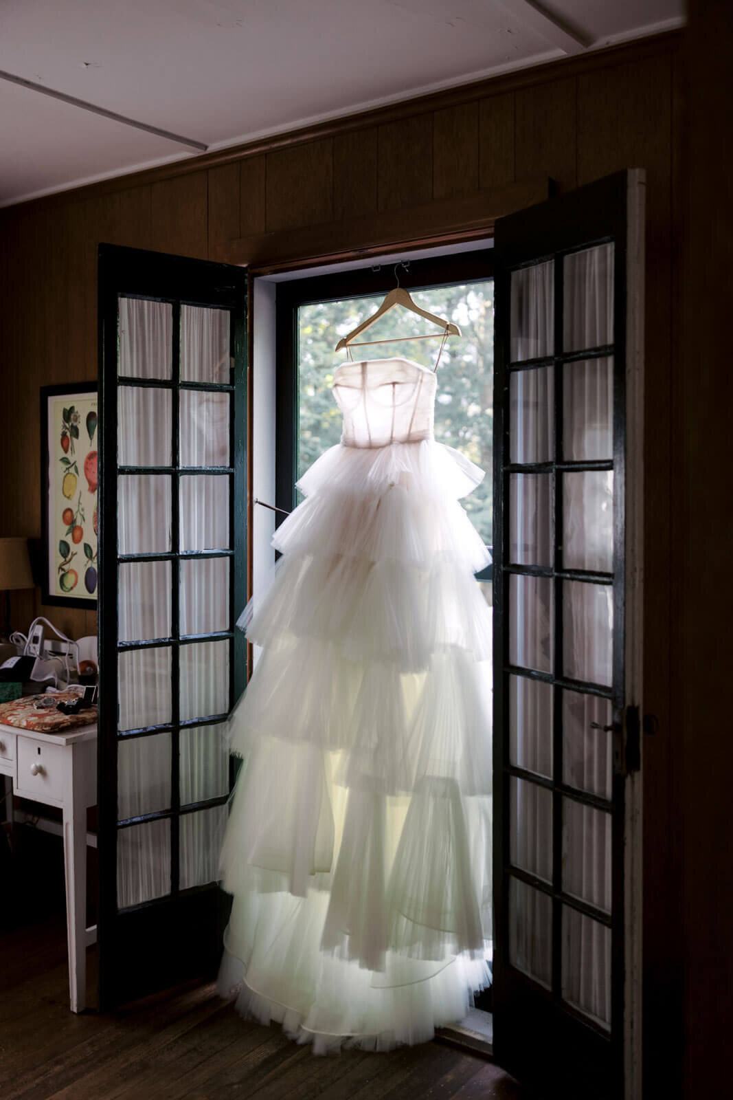 The bride's wedding dress is hung in the middle of two open doors in a room at The Ausable Club, New York.