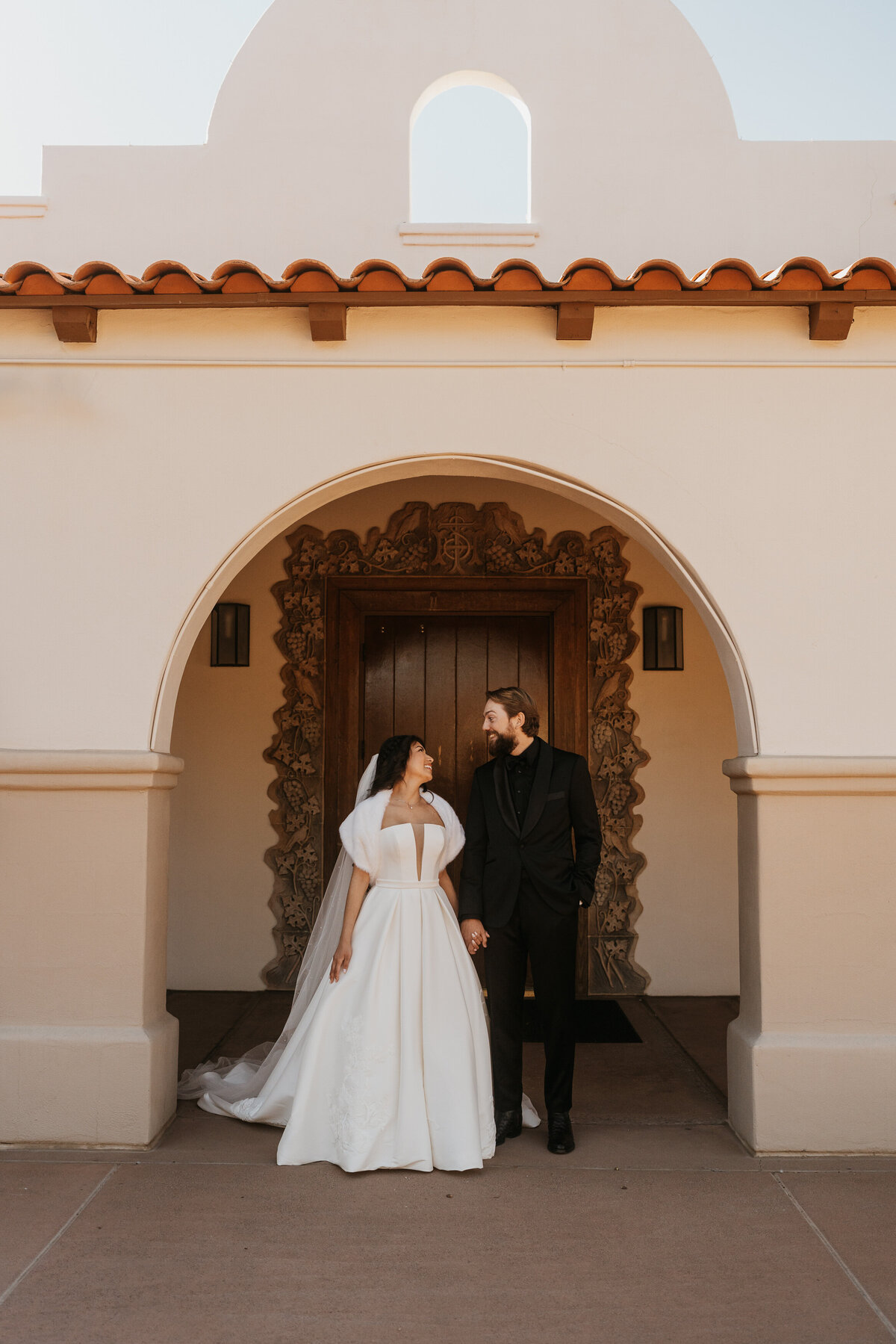 a newlywed couple standing side by side smiling at each other 