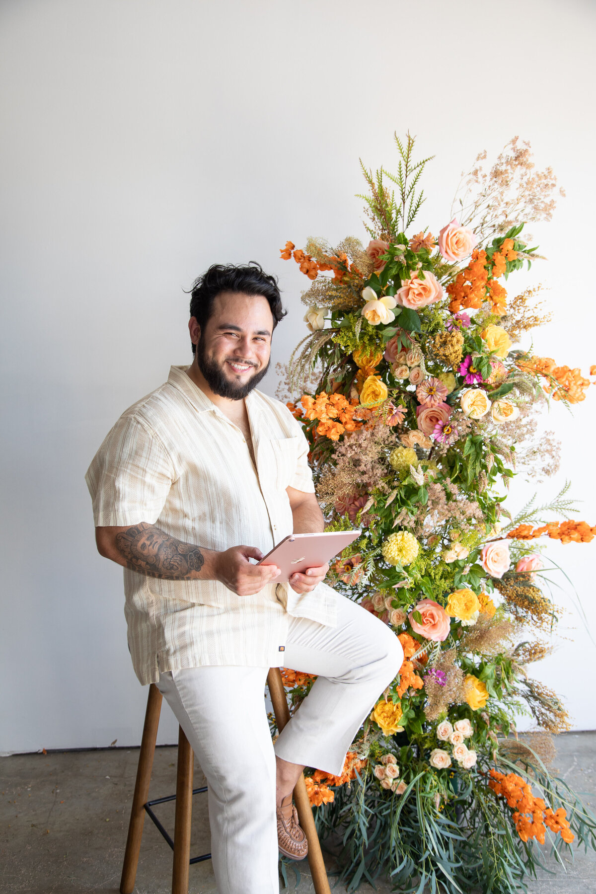 A man sitting on a stool next to a flower tower as captured by an Austin wedding photographer.