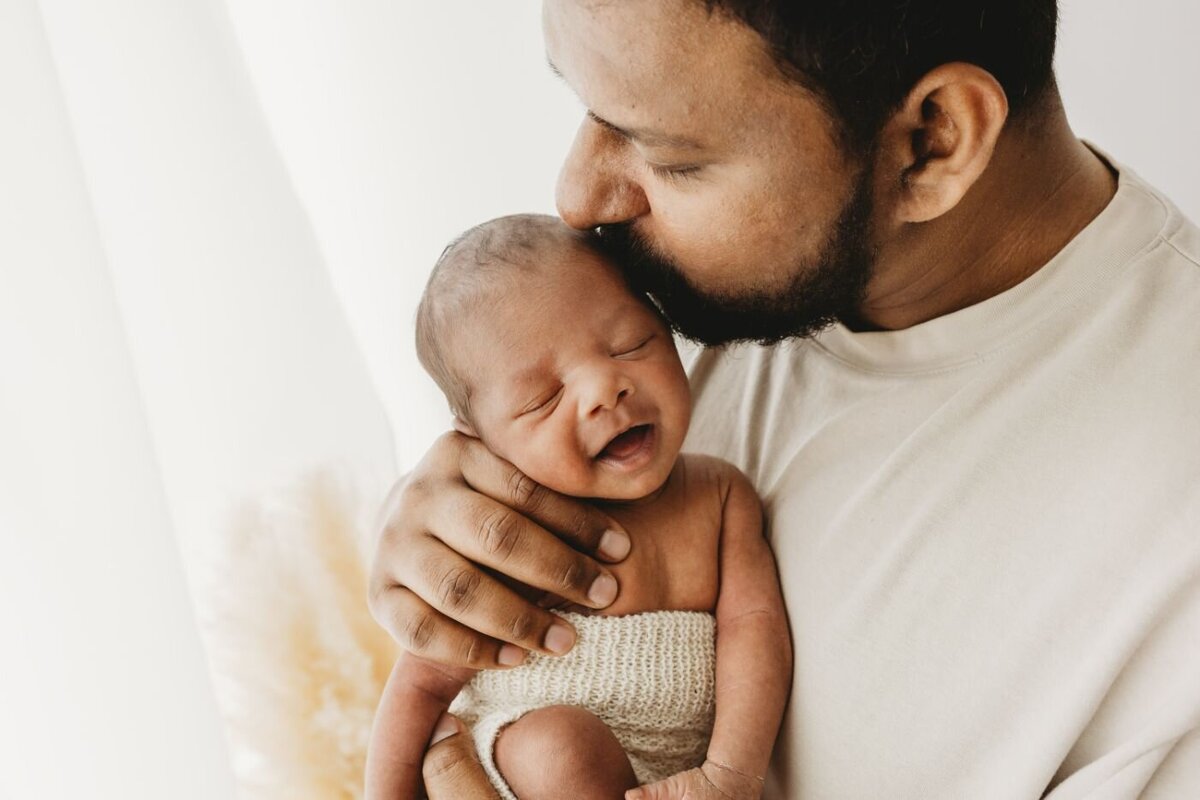 A heartwarming image of a father cradling his peacefully sleeping newborn baby, sharing a sweet kiss. Newborn photography by Ruaa Hamdan in the UK.