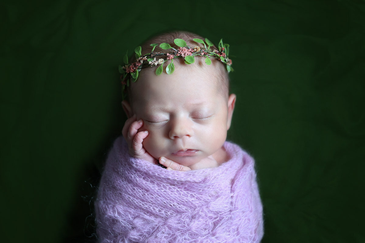 Newborn baby wrapped in purple blanket with flower hairband sleeping at home in Bearspaw Alberta photo session 