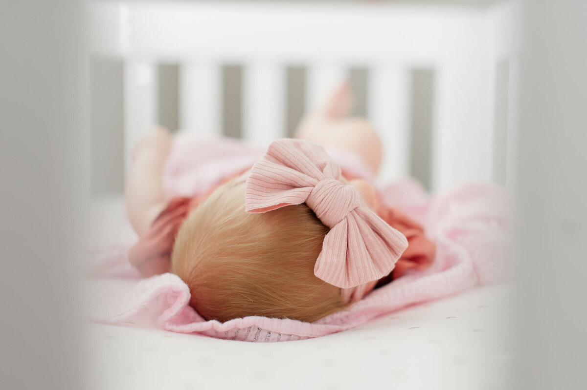 Closeup image of newborn baby laying in her crib with a pink bow on