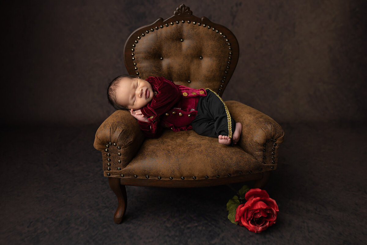 Baby dressed in a regal velvet outfit sleeping on a miniature chair, captured by Dallas newborn photographer.
