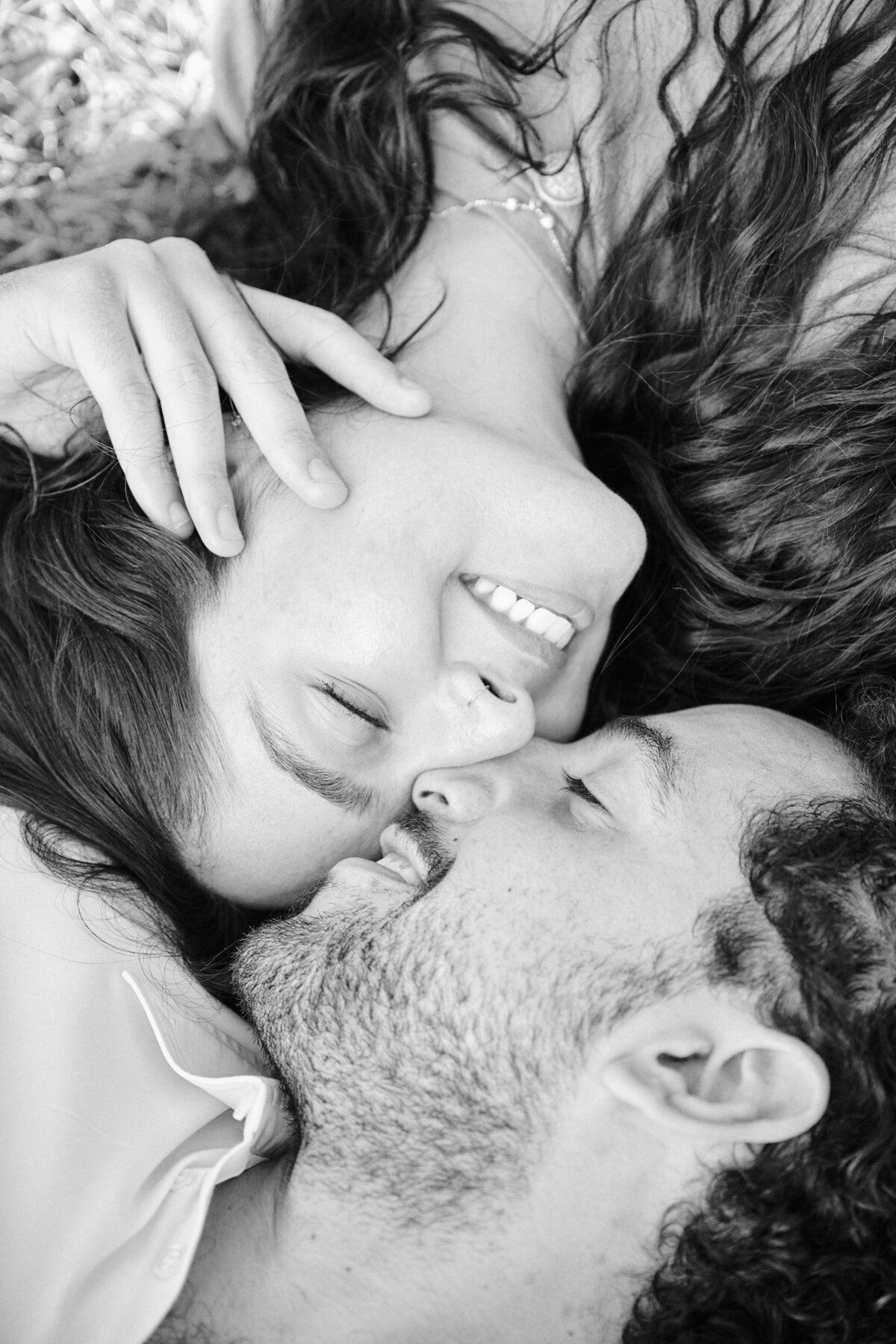 Black and white photo of a couple laying down on grass.  Faces nestled together  happily after a successful Proposal in a Park in Queens, New York City.  Photo taken by Corey Lamar Photography