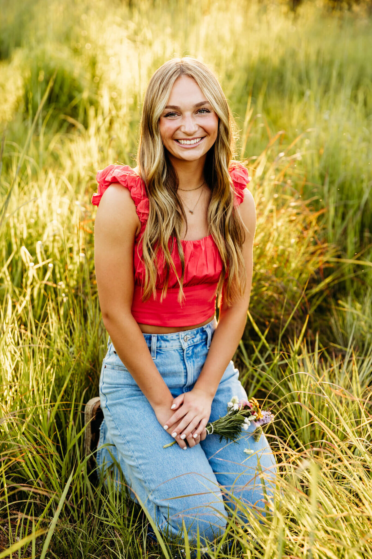 pretty teen girl in a cute red crop top and ruffle sleeves sitting on her knees in the grass with a small flower bouquet