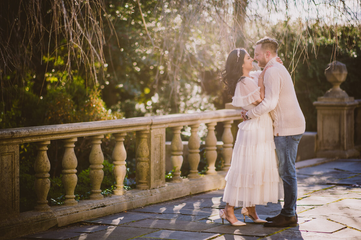 A couple sharing a moment wearing white fall clothing during their engagement session at the planting fields arboretum in oyster bay ny
