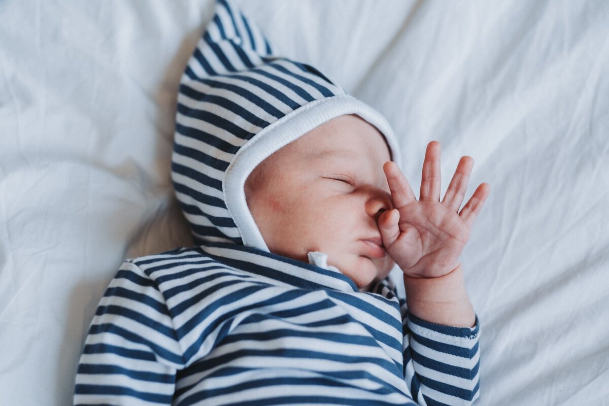 Sleeping newborn baby wearing a striped shirt and hat laying on white sheet